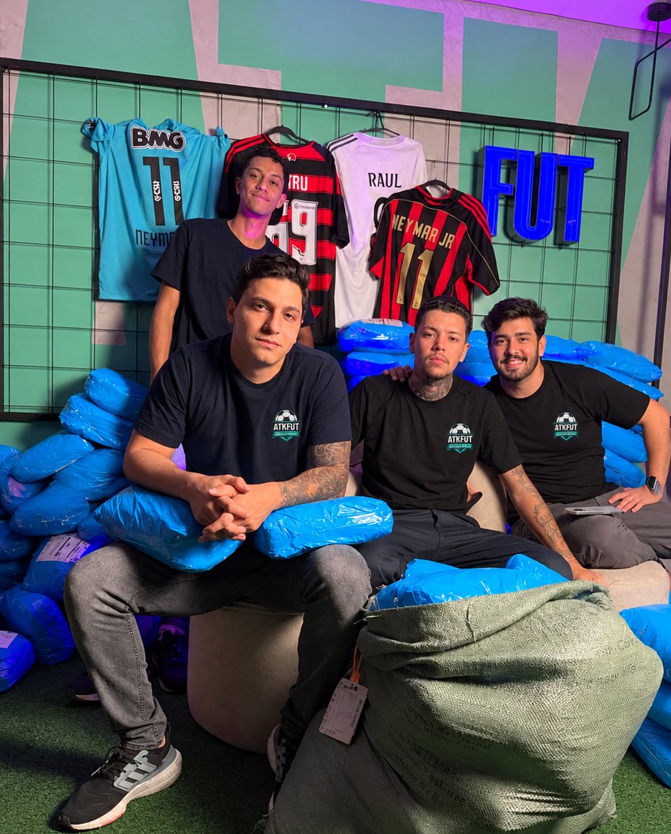 Equipe ATKFUT no estoque, com camisas na parede e pacotes prontos para envio